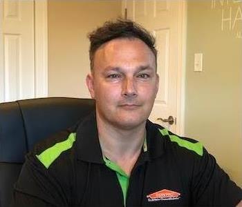 Male SERVPRO employee with a black shirt sitting down. 