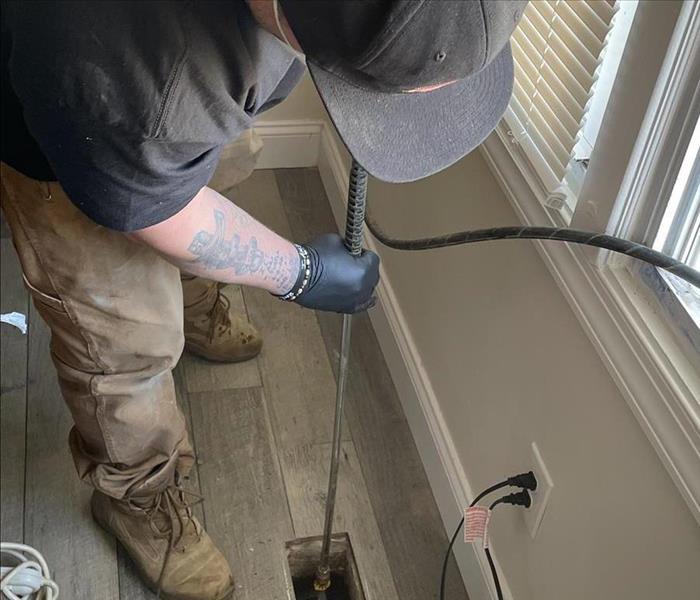 SERVPRO technician blasts water into floor vent using a pressure washer.