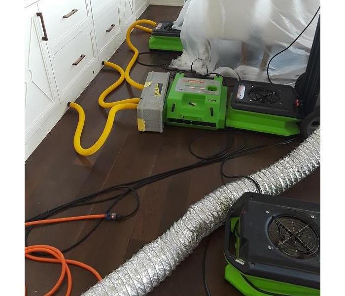 Green equipment on a hardwood floor with yellow tubes running into the baseboard. 