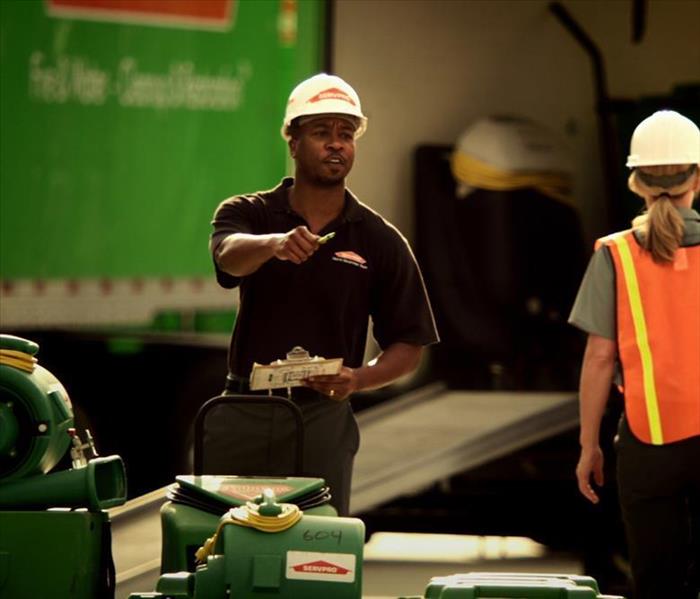 A SERVPRO employee in a white hard hat holds a pen and clipboard.
