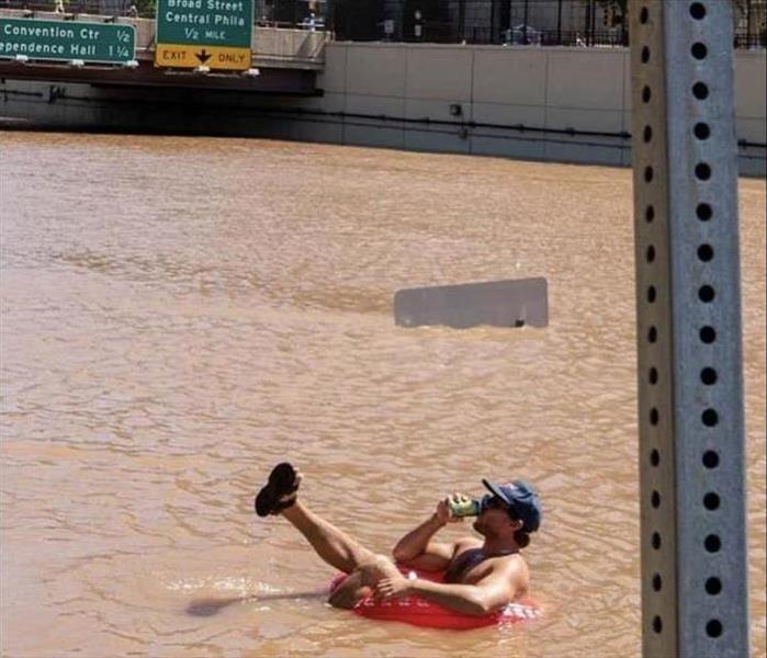 A man floats down the flooded Vine Street Expressway in Philadelphia while drinking a beer.