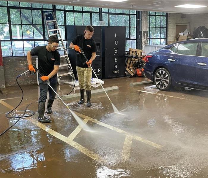 Two SERVPRO employees pressure wash the ground of a garage.