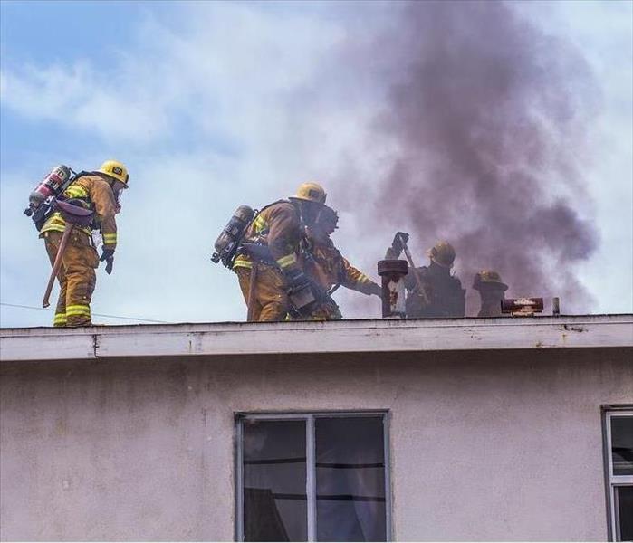 Firefighters on top of a home's roof battle smoke and flames.